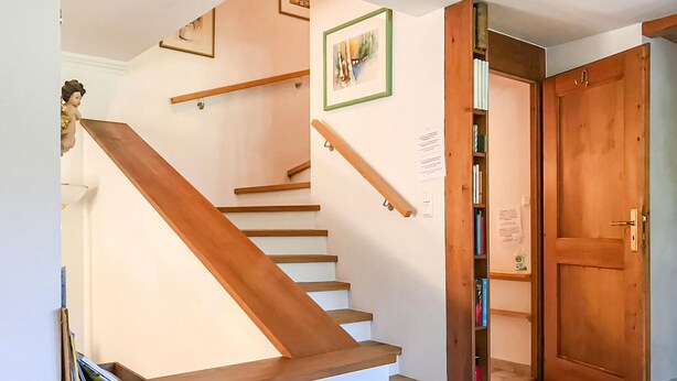 A wooden staircase with a handrail, a framed picture on the wall, and a door leading to a room with a bookshelf. - Beautiful home in Mondsee with house a mountain view (Mondsee)