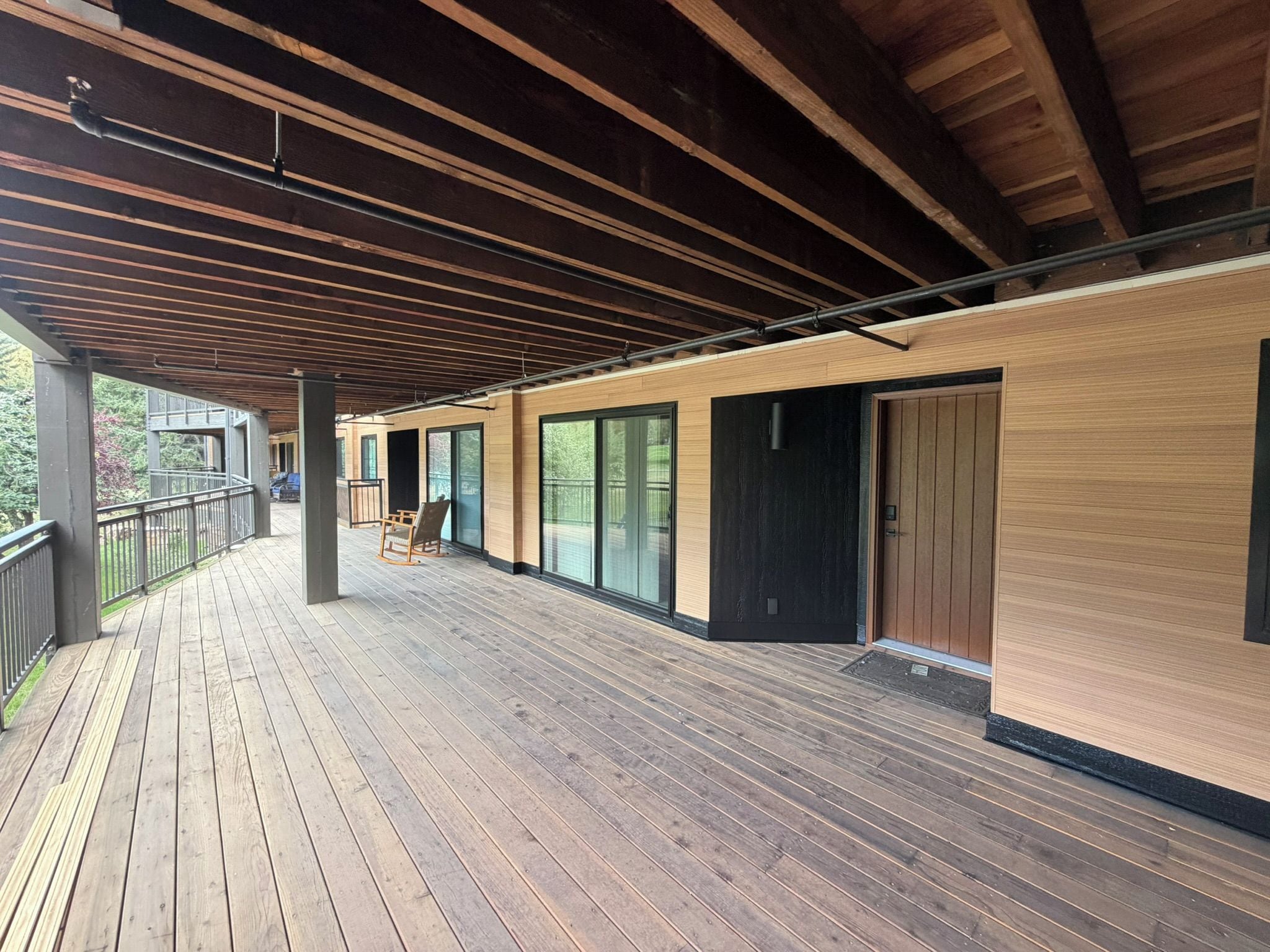 Une terrasse en bois couverte, dotée d’une rambarde, d’une porte en bois et d’une porte en verre.