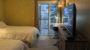 A hotel room with two beds, a desk with a television, and a view of a snowy balcony. - Luxury Condo; Just steps to PCMR & Historic Main St!! (Park City)