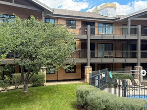 A multi-story building with balconies, a tree, and a fenced pool area.
