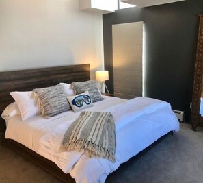 Un lit bien fait, avec des draps blancs, deux oreillers, un plaid et une lampe de chevet.