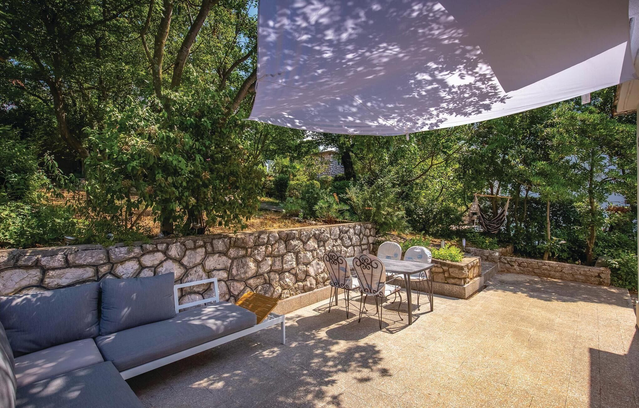 Un patio esterno con un muro in pietra, un divano grigio e un tavolo con sedie.