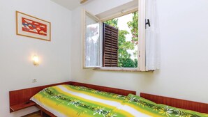 Una piccola stanza con un letto singolo, una finestra con persiane di legno, una lampada a parete e un quadro incorniciato.