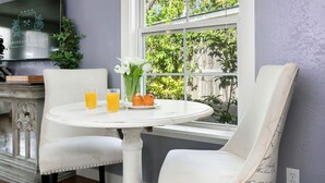 A dining area with a round table, two chairs, a vase with flowers, and two glasses of orange juice. - Bella Manor Lavender Suite | King Bed | Walk to Main (Fredericksburg)
