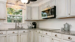 A kitchen with white cabinetry, a stainless steel microwave, a coffee maker, and a chandelier. - Bella Manor Lavender Suite | King Bed | Walk to Main (Fredericksburg)