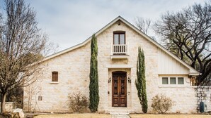 A stone building with a central entrance, a small balcony, and two tall trees in front. - Bella Manor Lavender Suite | King Bed | Walk to Main (Fredericksburg)