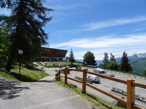A parking area with a building, a wooden fence, and a view of mountains.