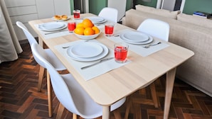 Een eettafel gedekt met borden, bestek en een schaal met mandarijnen, en een rood drankje op tafel.
