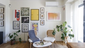 Een woonkamer met een bank, stoelen, een salontafel en diverse ingelijste kunstwerken aan de wanden.