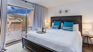 A hotel room with a large bed, a view of a mountainous landscape, and a balcony with outdoor seating.