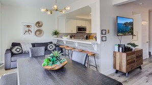 A modern kitchen with white cabinets, a microwave, and a large island with stools.