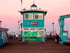 Un puesto de mariscos con un letrero que dice 'SEAFOOD FISH AND CHIPS' y 'PARASAILING' en un muelle.