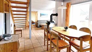 Un comedor con mesa y sillas de madera, una escalera y una zona de cocina con una parrilla.