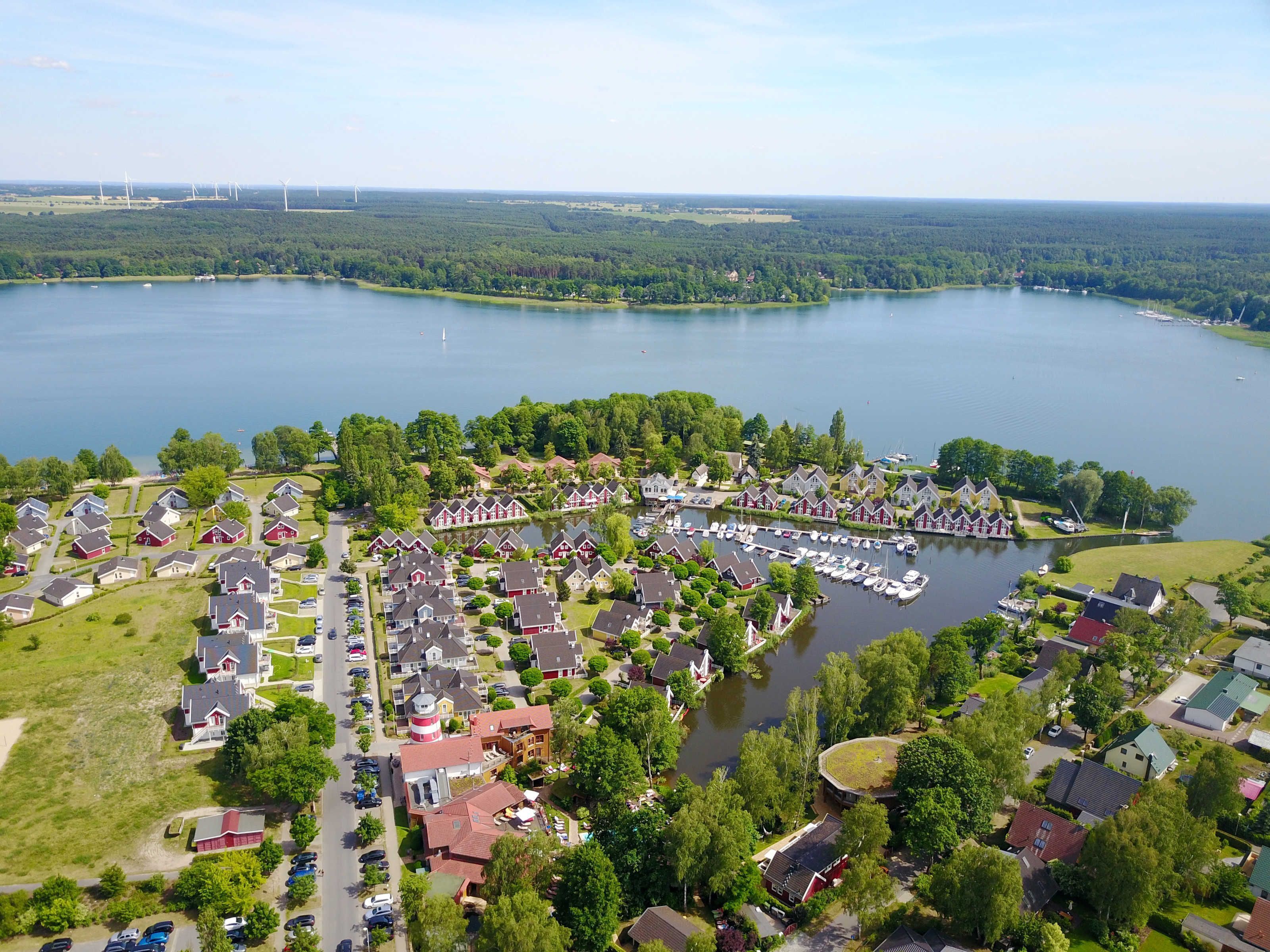 An aerial view of a lakeside residential area with houses, a marina, and wind turbines in the distance.