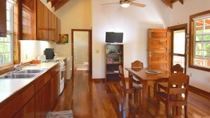 Cocina compacta con gabinetes de madera, una mesa de comedor con sillas, un ventilador de techo y un televisor montado en la pared.