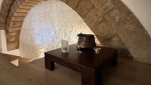Ein steinerner Bogen führt zu einem Raum mit einem Holztisch, einem Metalltopf und zwei Weingläsern.