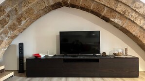 Ein modernes Wohnzimmer mit einem Steingewölbe, einem Flachbildfernseher auf einem dunklen Holz-TV-Möbel, einer roten Vase und einem Glas mit einem Holzstäbchen.
