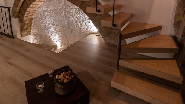 Ein modernes Interieur mit einer Holztreppe, einem steinernen Bogen und einem dunklen Holztisch mit einer Schale Snacks.