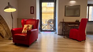 Ein Zimmer mit einem roten Sessel, einer Stehlampe, einem Esstisch und einem großen Spiegel an der Wand.