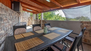 An outdoor patio with a stone wall, a grill, wicker chairs, and a table with placemats.