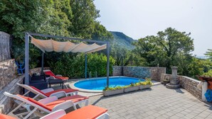 A pool area with lounge chairs, a pergola, and a stone wall.