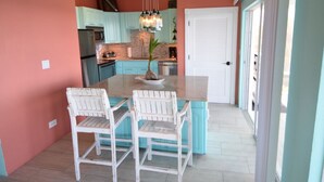 Une cuisine avec des meubles de couleur turquoise, un îlot central doté de chaises et un luminaire suspendu.