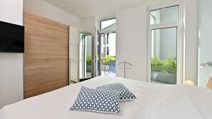 Habitación de hotel moderna con una cama grande, dos almohadas estampadas, un cabecero de madera y ventanas amplias que ofrecen vistas al exterior.