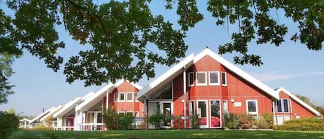 Een rood gebouw met een schuin dak, omgeven door groen gras en bomen.