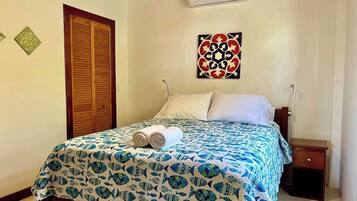 A bedroom with a bed, a nightstand, an air conditioning unit, and a decorative wall piece.