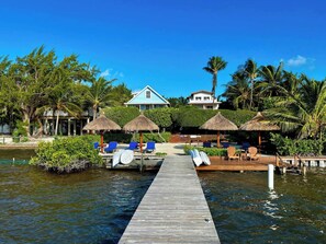 A wooden dock leading to a beach area with lounge chairs and thatched umbrellas. - Oceanfront Unit w/dock/pool/AC-free paddle boards -2 bed, 1 bath sleeps 6 (Caye Caulker)