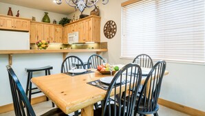 Un coin repas avec une table et des chaises en bois, un lustre et une fenêtre équipée de stores.