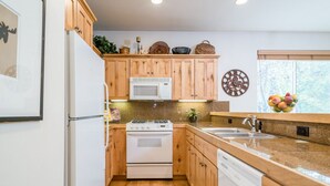 Une cuisine avec des meubles en bois, un four à micro-ondes, une cuisinière, un lave-vaisselle et une fenêtre donnant sur des arbres.