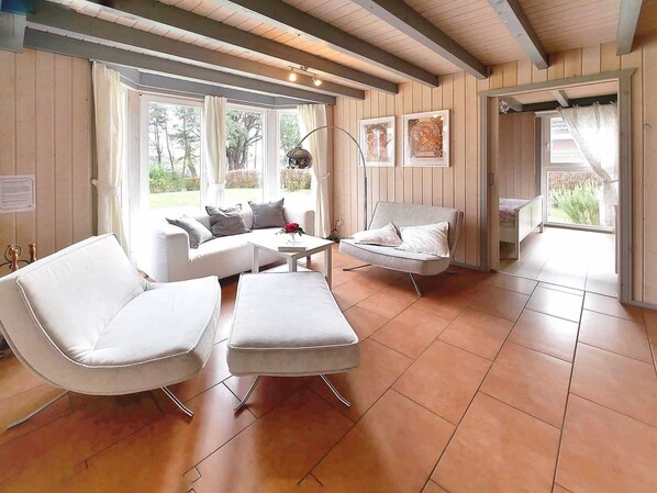 A modern living room with a sofa, two armchairs, a coffee table, and a dining table. There are large windows with curtains, a ceiling with exposed beams, and artwork on the walls. - Seeperle with whirlpool incl. additional costs - Ferienpark Scharmützelsee (Wendisch Rietz)