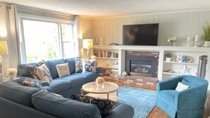 Ein Wohnzimmer mit einem blauen Sofa, einem blauen Sessel, einem Kamin und einem Bücherregal.