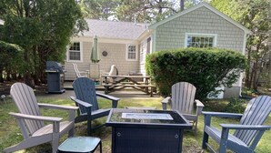 Ein Garten mit Adirondack-Stühlen, einem Glastisch und einem kleinen Schuppen.