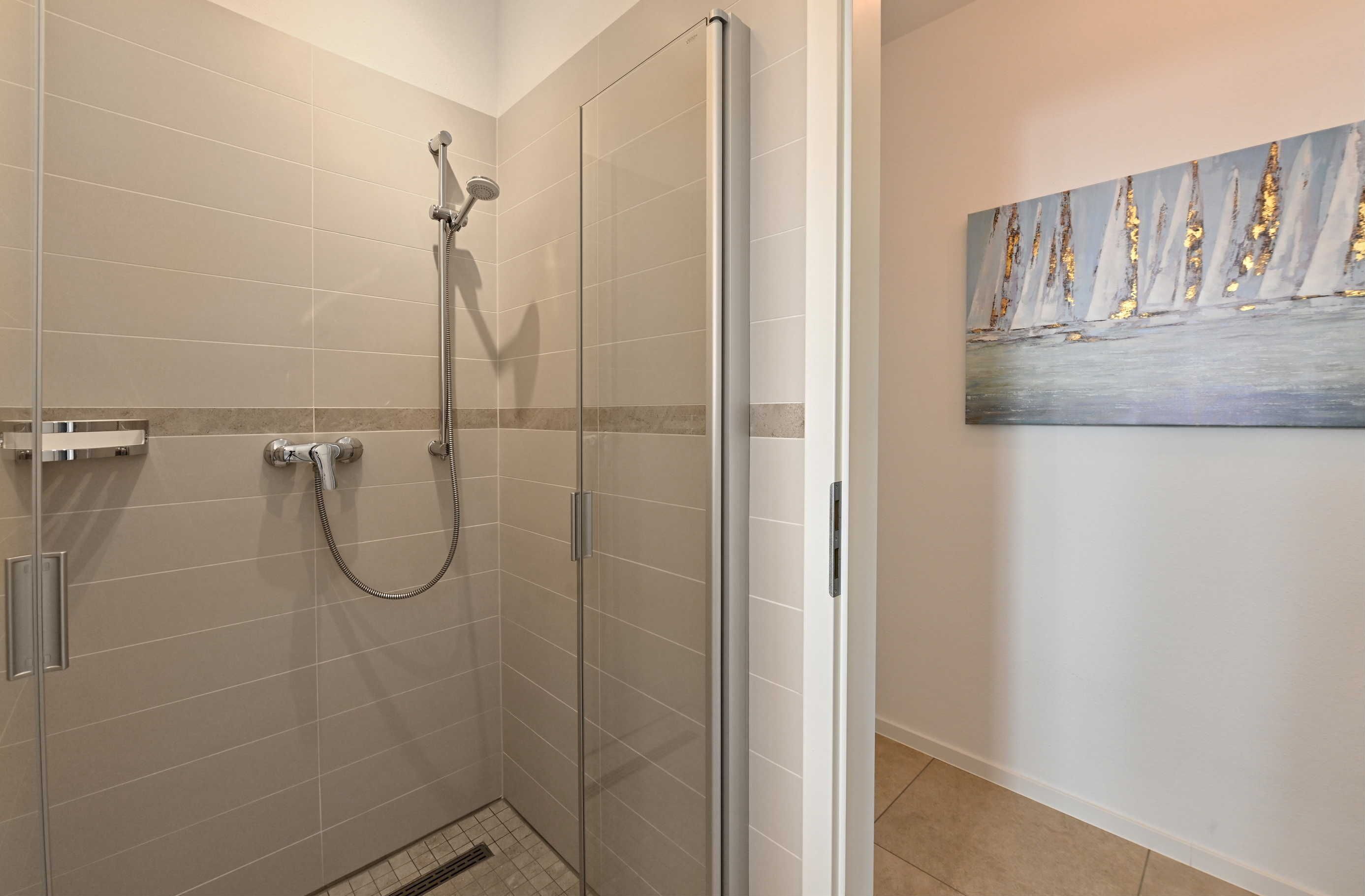 Une douche fermée par des parois en verre, dotée d’un pommeau de douche à main et d’un robinet mural.
