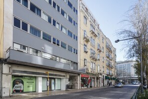 A multi-story building with a modern facade, a ground-level shop, and a street with cars and pedestrians.