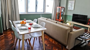 Een eetgedeelte met een tafel gedekt voor twee personen, een bank en een televisie in een kamer met groene wanden en houten vloeren.