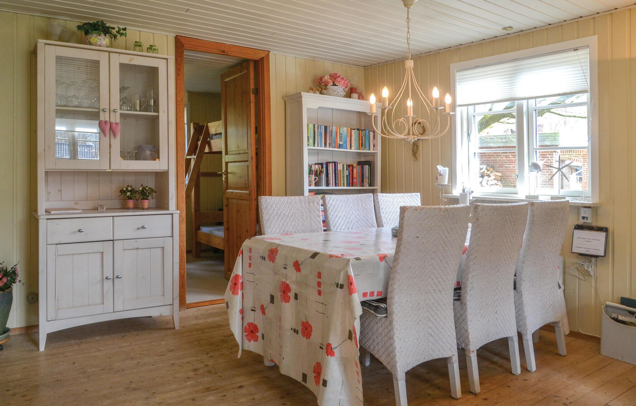 Un'area pranzo con un tavolo ricoperto da una tovaglia floreale, circondato da quattro sedie decorate. Si intravede sullo sfondo una libreria piena di libri.