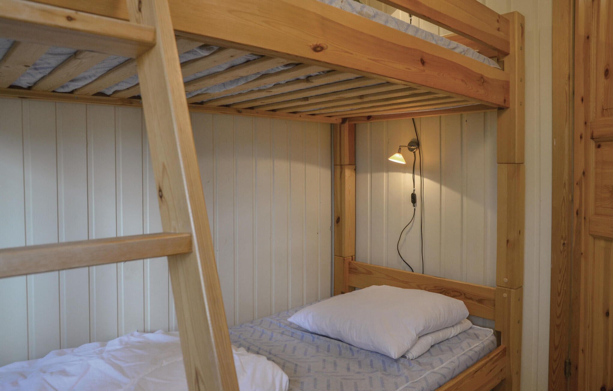 Et soveværelse med køjeseng, træloft og trævægge, en enkeltseng med pude og en lampe monteret på væggen.
