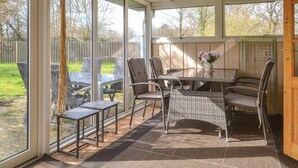 Eine überdachte Terrasse mit Tisch und Stühlen, großen Fenstern und Blick auf den Garten.