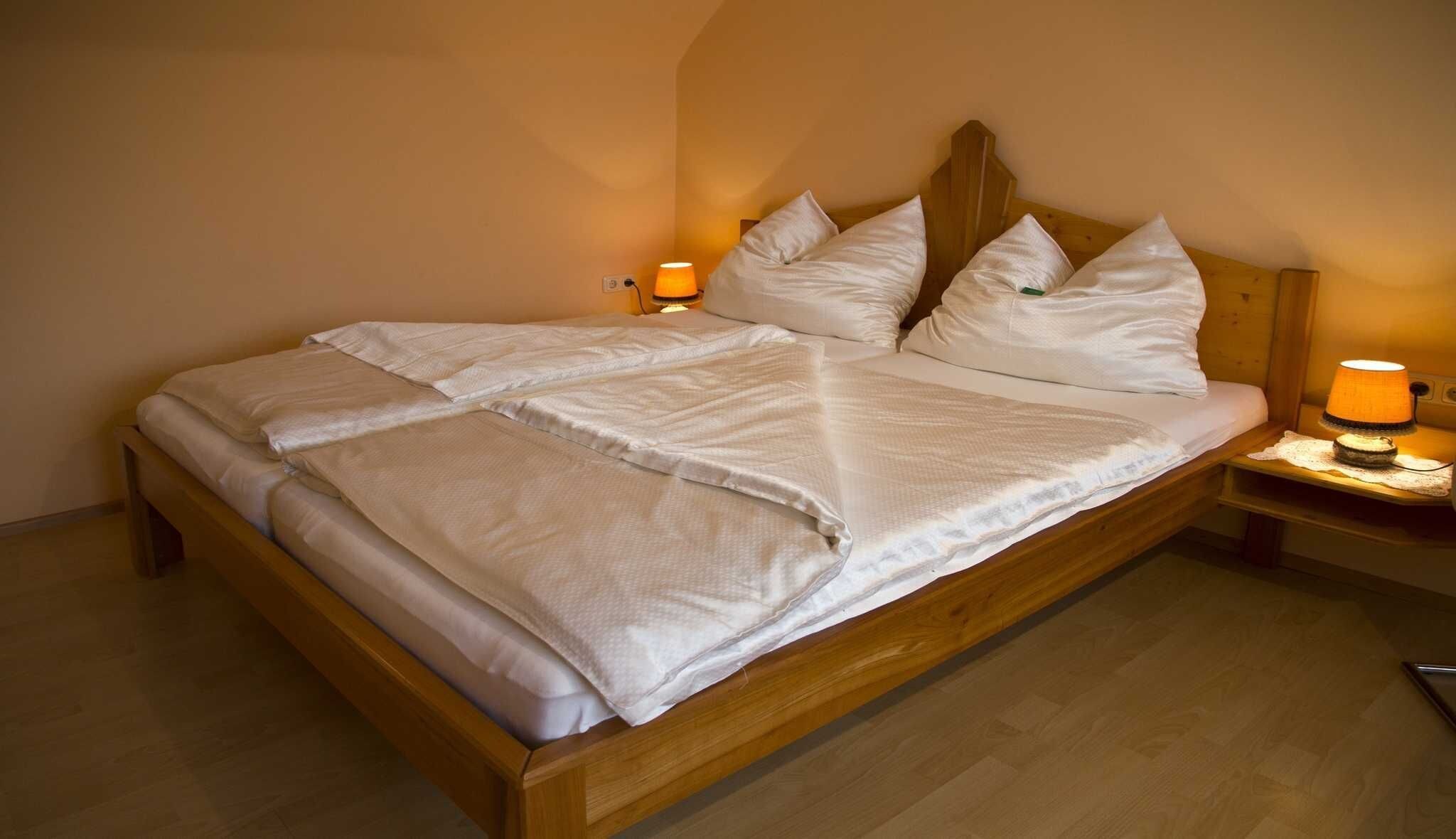 A neatly made bed with white linens, two bedside lamps, and a wooden headboard.