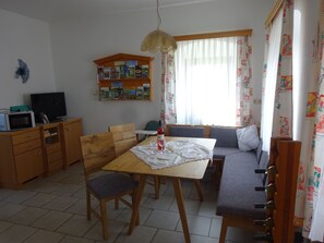 Un comedor con una mesa de madera, sillas, un sofá, televisión, estantería y una ventana con cortinas.