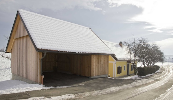 A wooden building with a sloped roof, a covered entrance, and a paved driveway. - Vacation cottage - Ermi/Pracher (Petzelsdorf in der Weststeiermark)