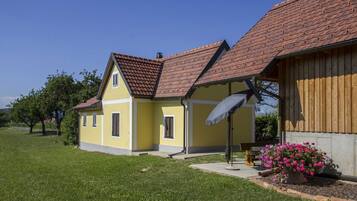 A yellow building with a red-tiled roof, a covered porch, and a bench with flowers.