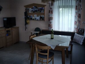 A small dining area with a table, chairs, a television, and a shelf with photos.