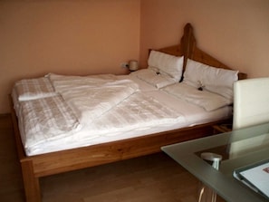 A bed with a wooden headboard, a bedside table, and a nightstand with a lamp. - Vacation cottage - Ermi/Pracher (Petzelsdorf in der Weststeiermark)