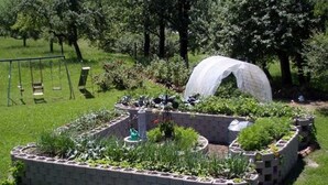 Ein Garten mit erhöhten Beeten, einer Schaukel und einem überdachten Bereich.