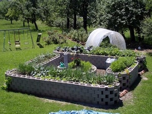 Un giardino con aiuole rialzate, altalene e una struttura coperta.