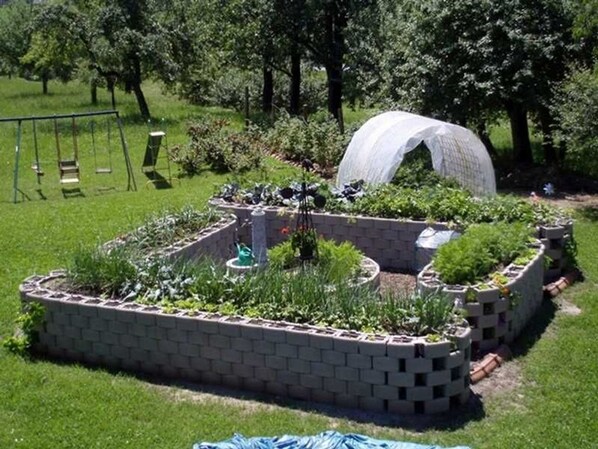Un jardín con camas elevadas, un parque infantil y una estructura cubierta.
